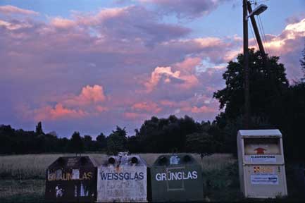 Altglasbehaelter am Abend vor Wiesen und Baeumen